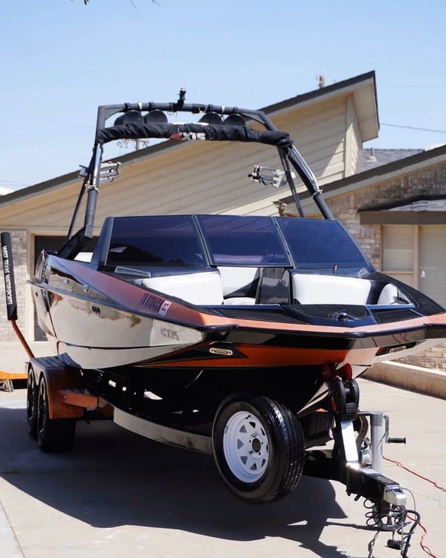Wake boat on a trailer in a residential driveway, front three-quarter view